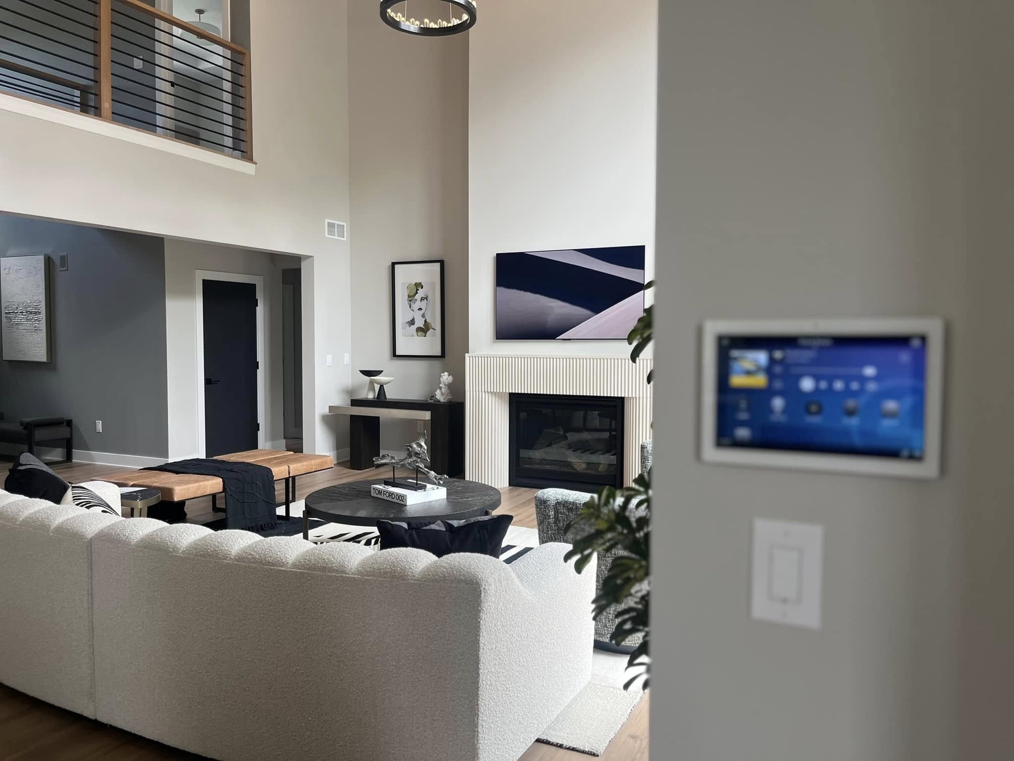 A wall mounted touchscreen showing a control menu, just off a living room with a fireplace and sectional sofa.